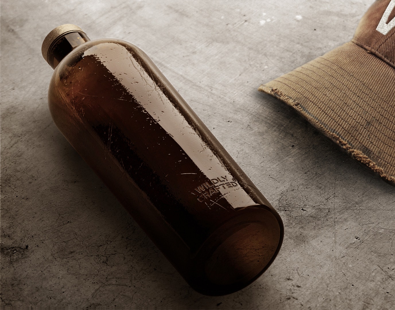 Estal Wildly Crafted Slika razpoloženja: rjava steklenica kolekcije Wildly Crafted leži na sivi betonski podlagi, poleg nje rjav pokrovček s šilom
